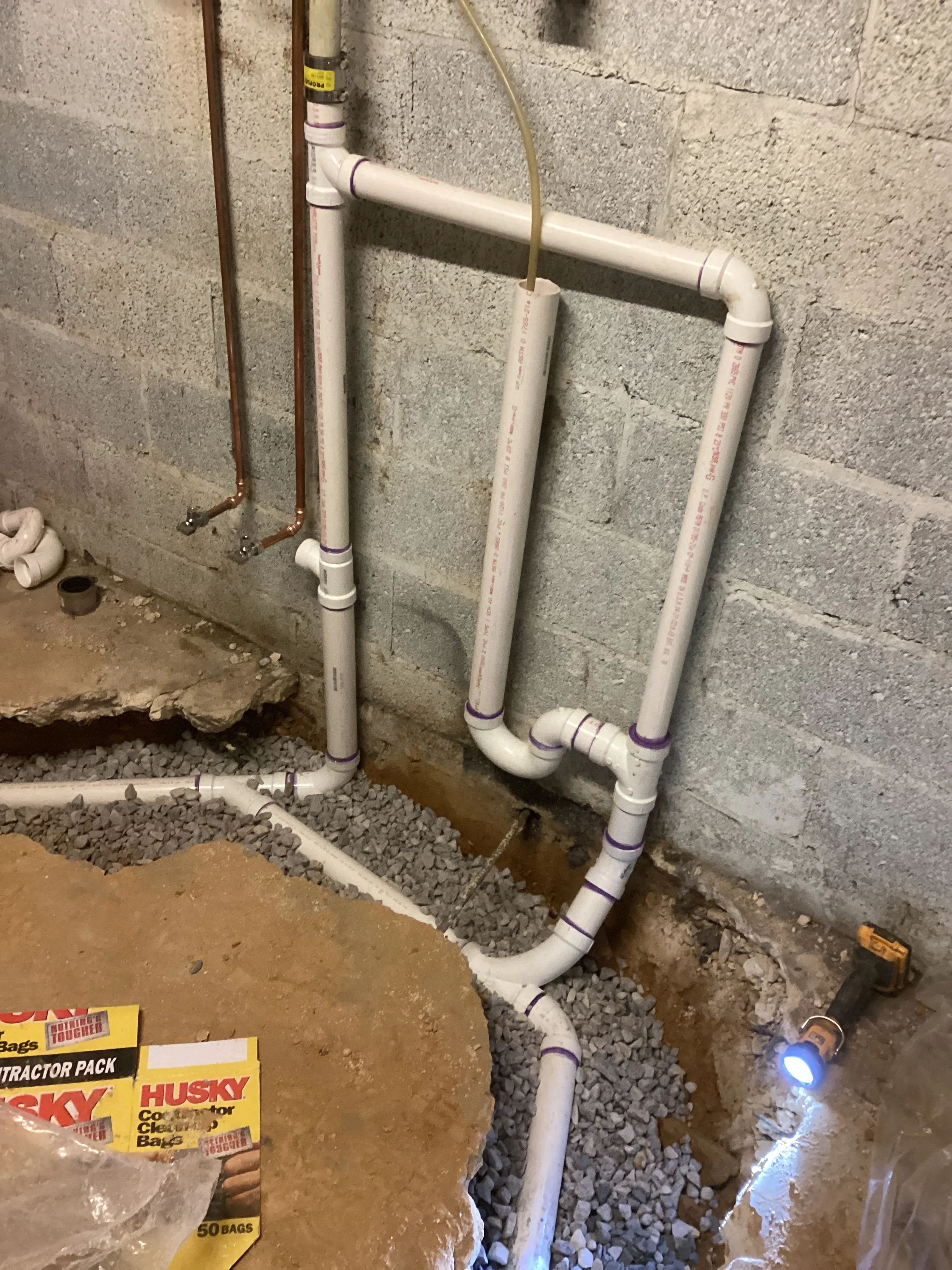 White PVC drain pipes installed in basement with gravel base and labeled connections