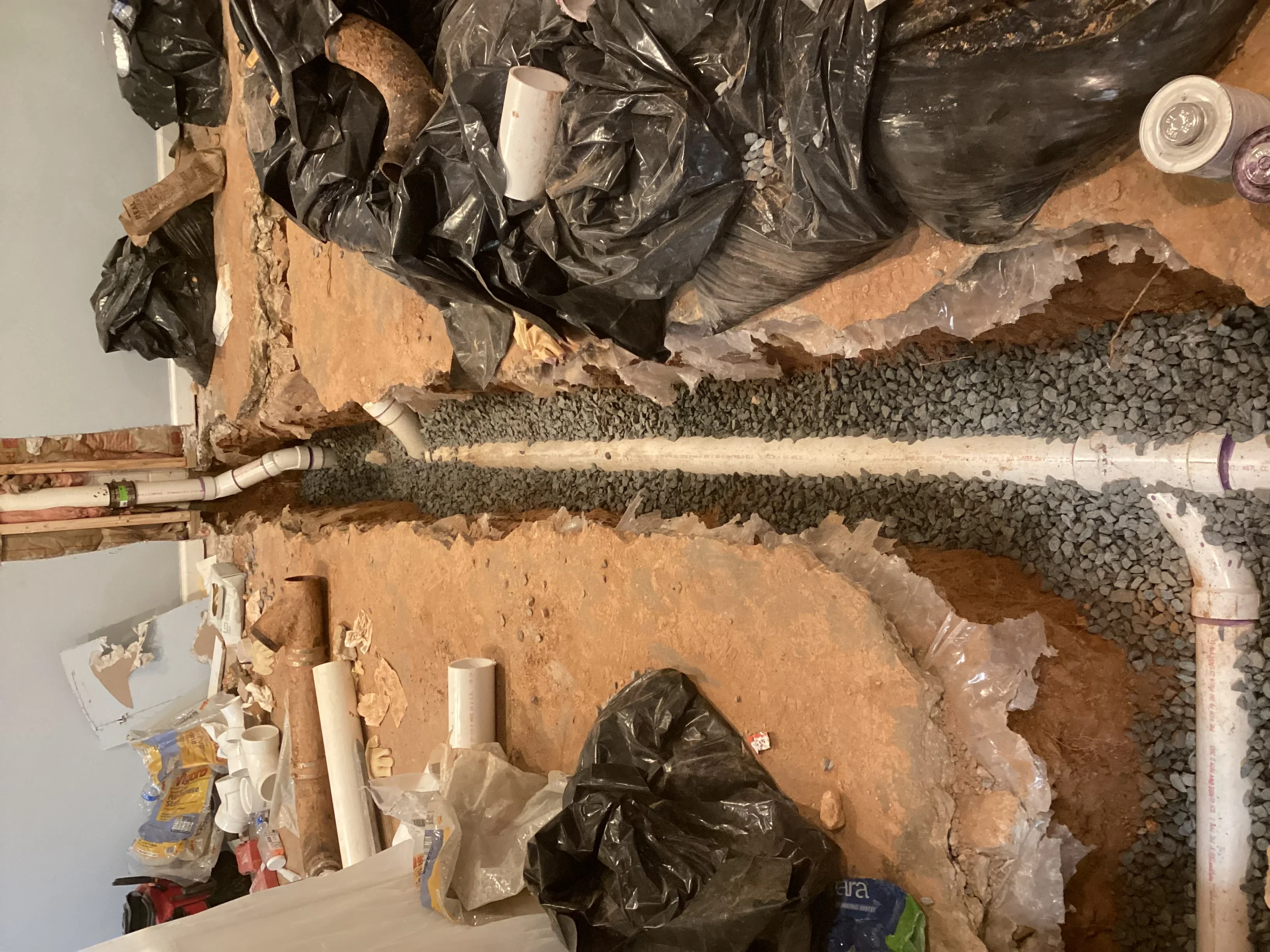 Foundation drain installation with PVC pipe, gravel bed, and protective black membrane during construction