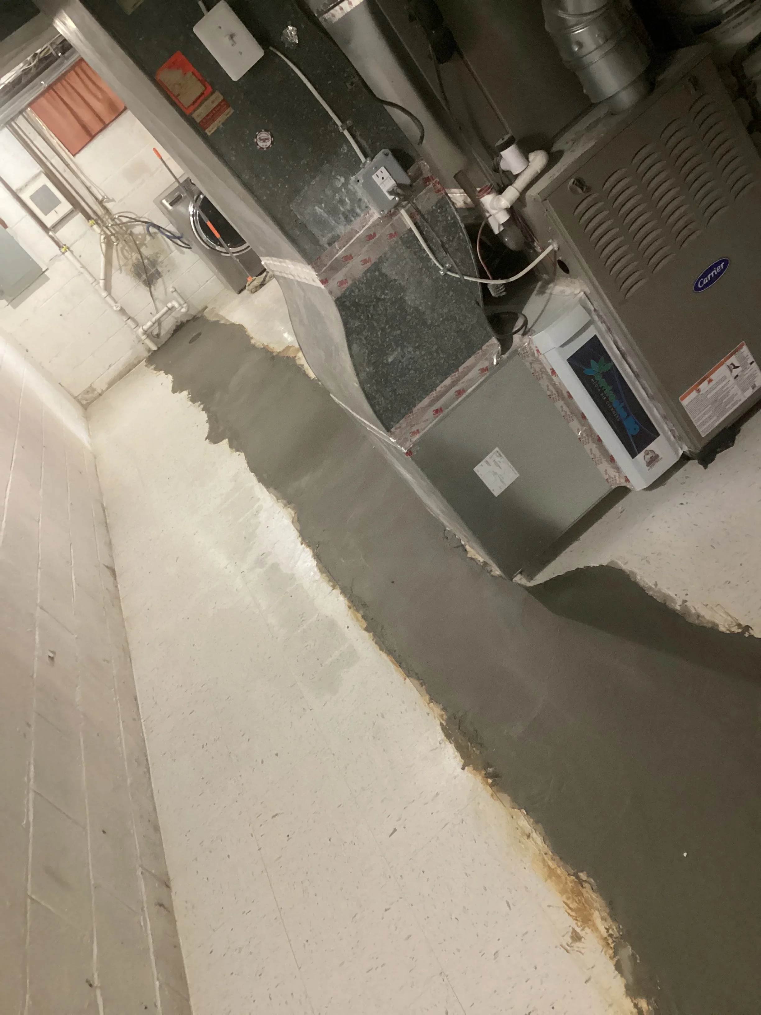 Overhead view of installed Carrier HVAC unit with plumbing connections and ductwork in utility space