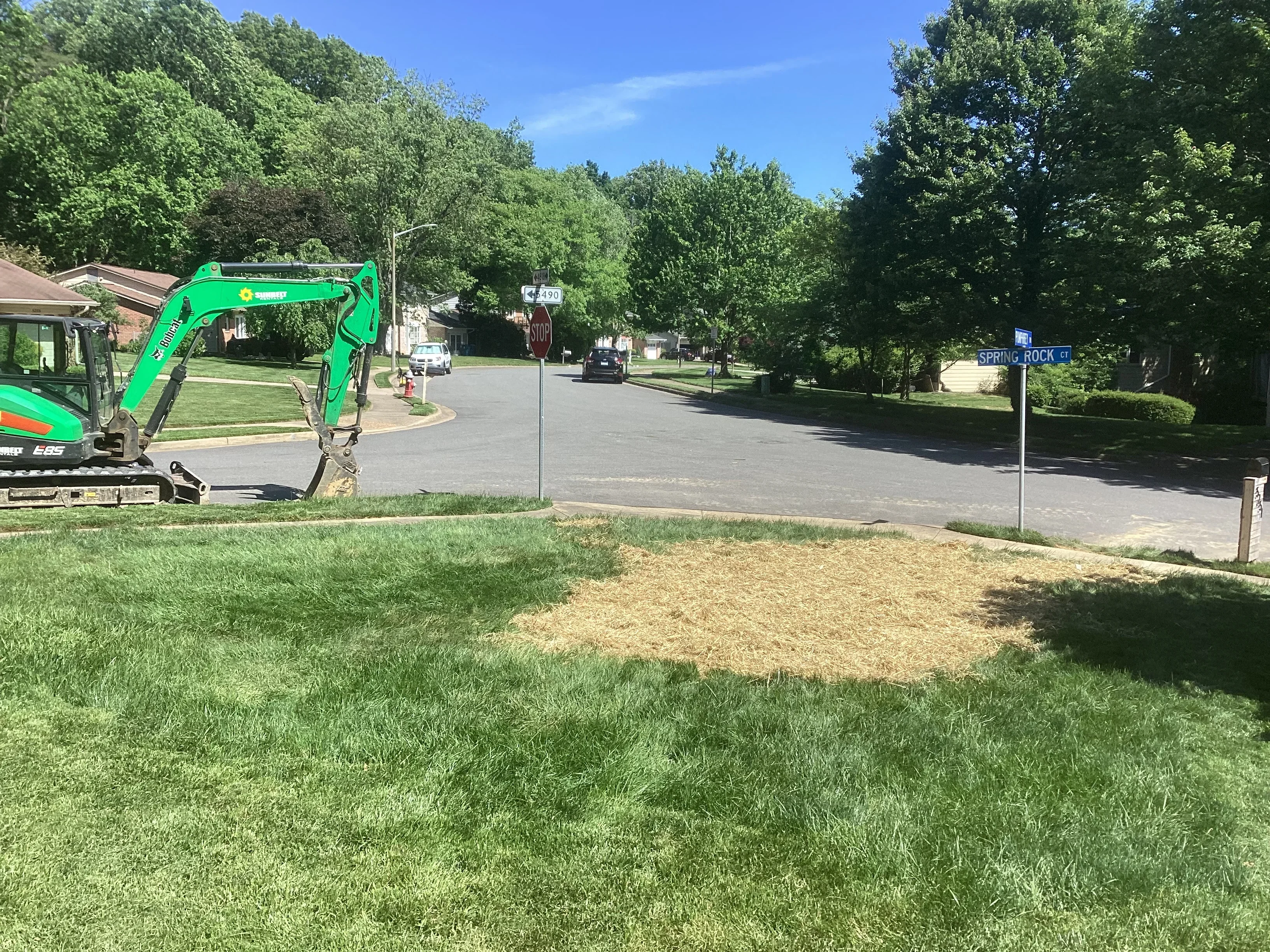 Green compact excavator on residential lot during underground utility line excavation project