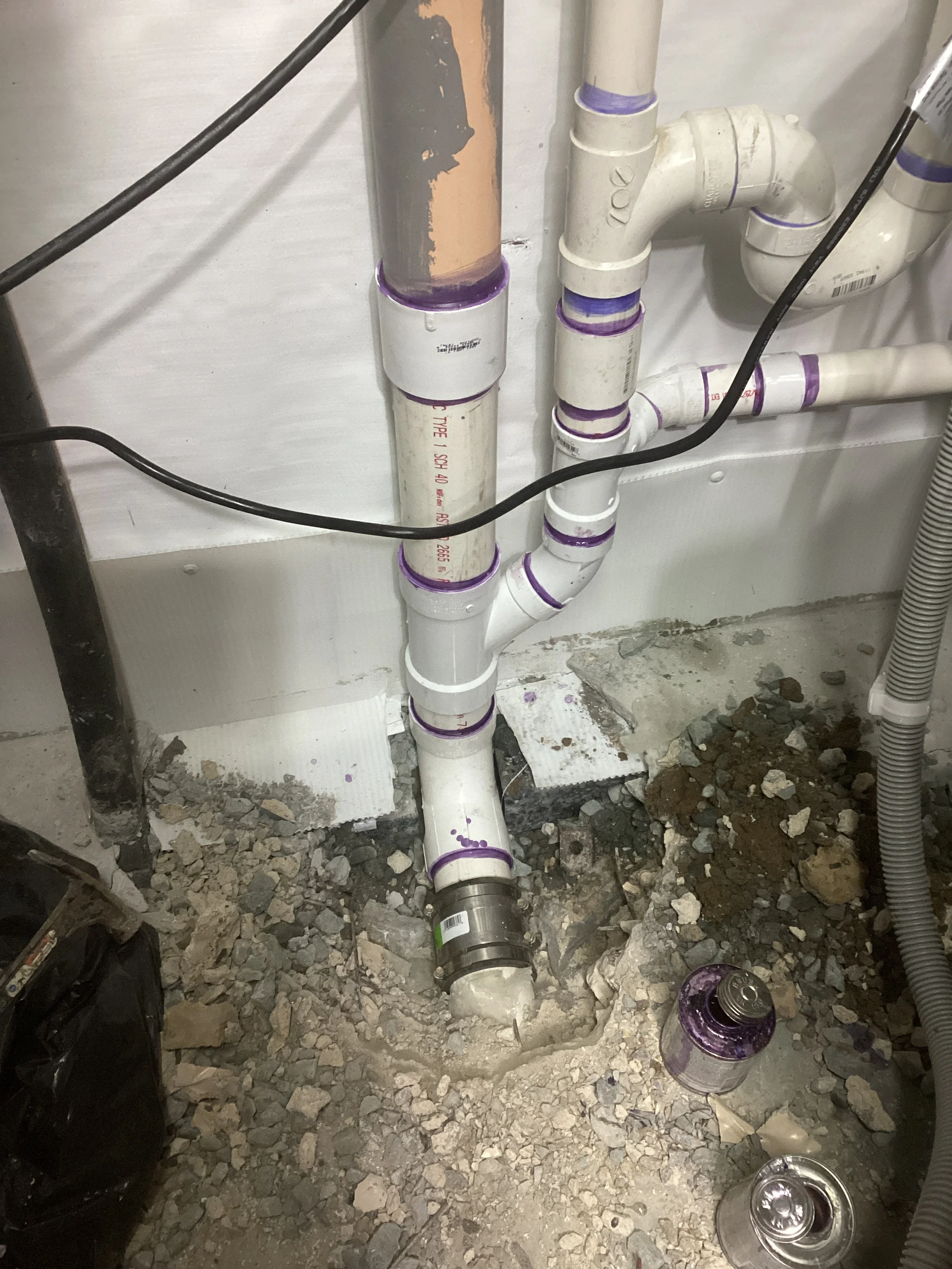 Installed sump pump system with white PVC pipes and purple connectors in basement