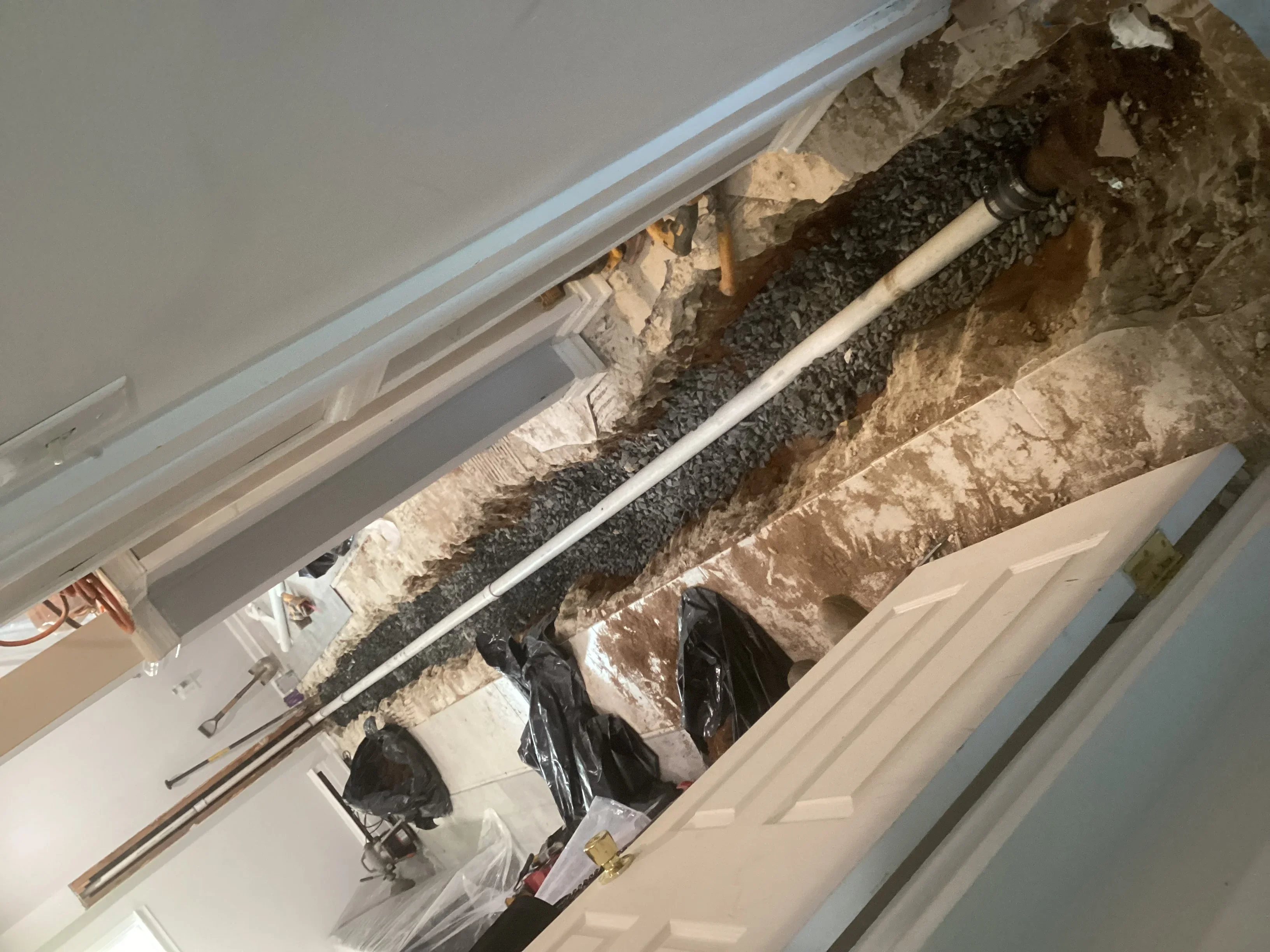 Basement drain line installation with PVC pipe, gravel base, and protective wrapping