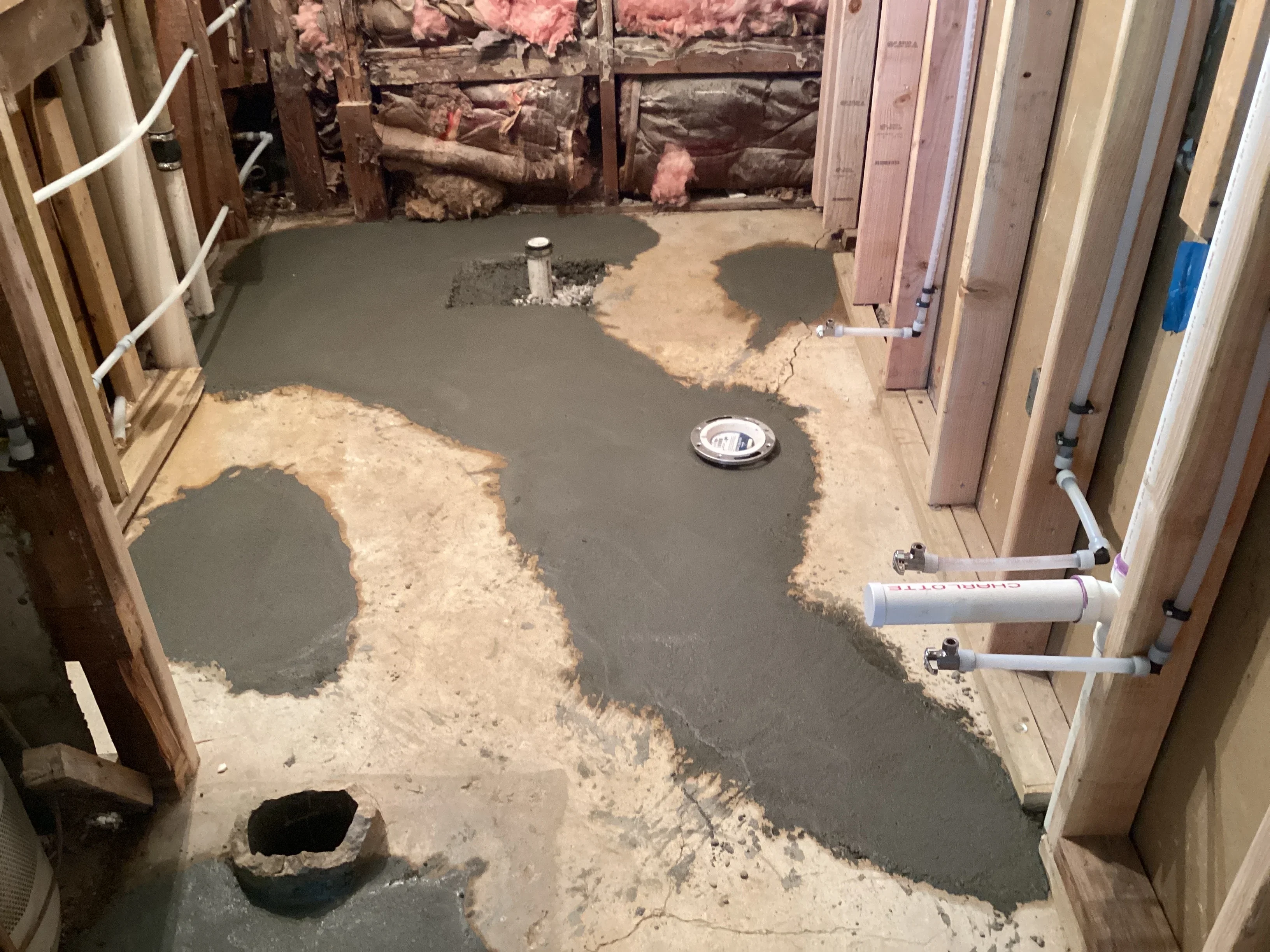 Wet concrete basement floor with plumbing pipes and drain fixtures during installation