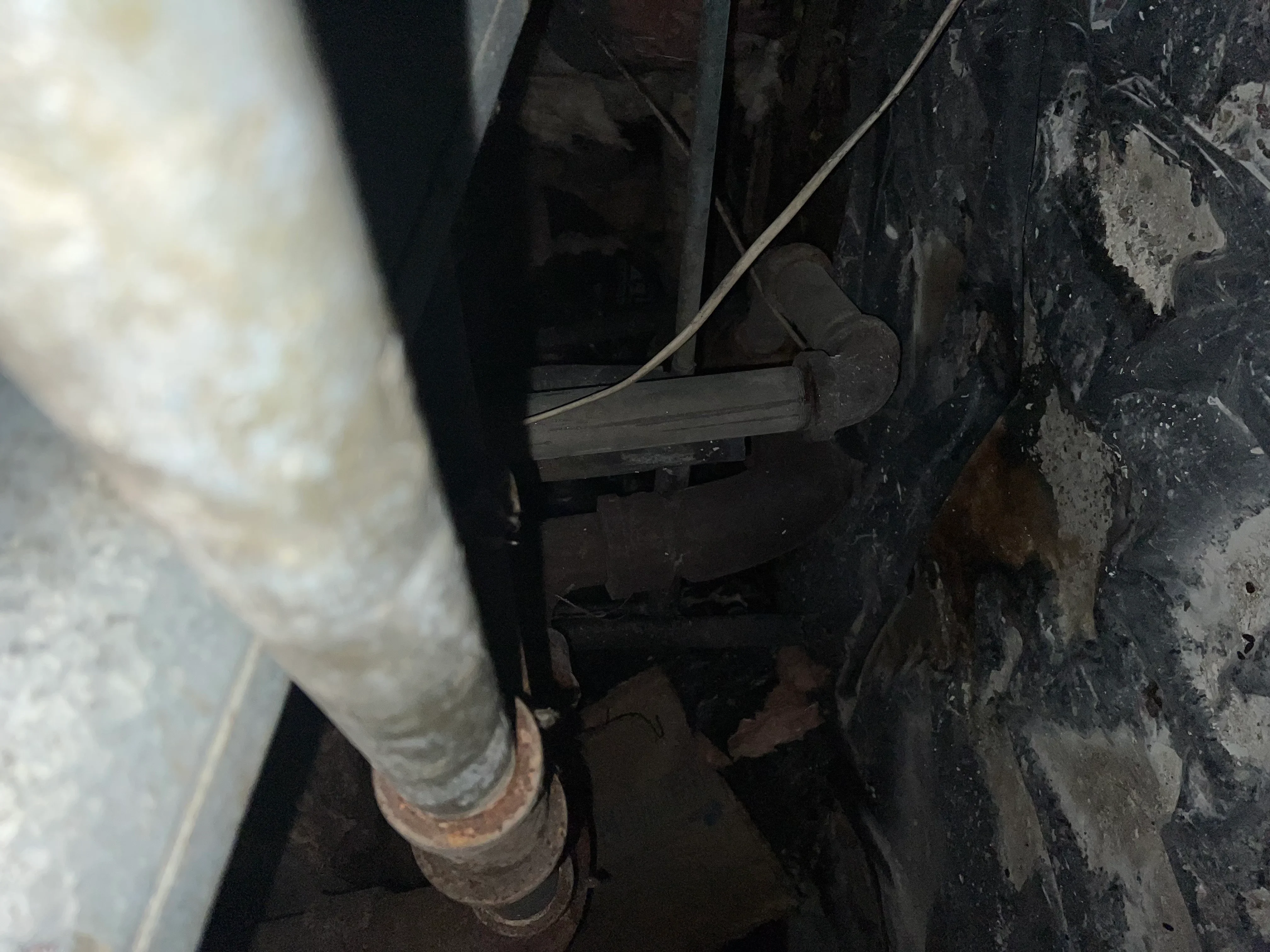 Close-up of corroded downspout elbow repair at foundation with metal bracket securing connection