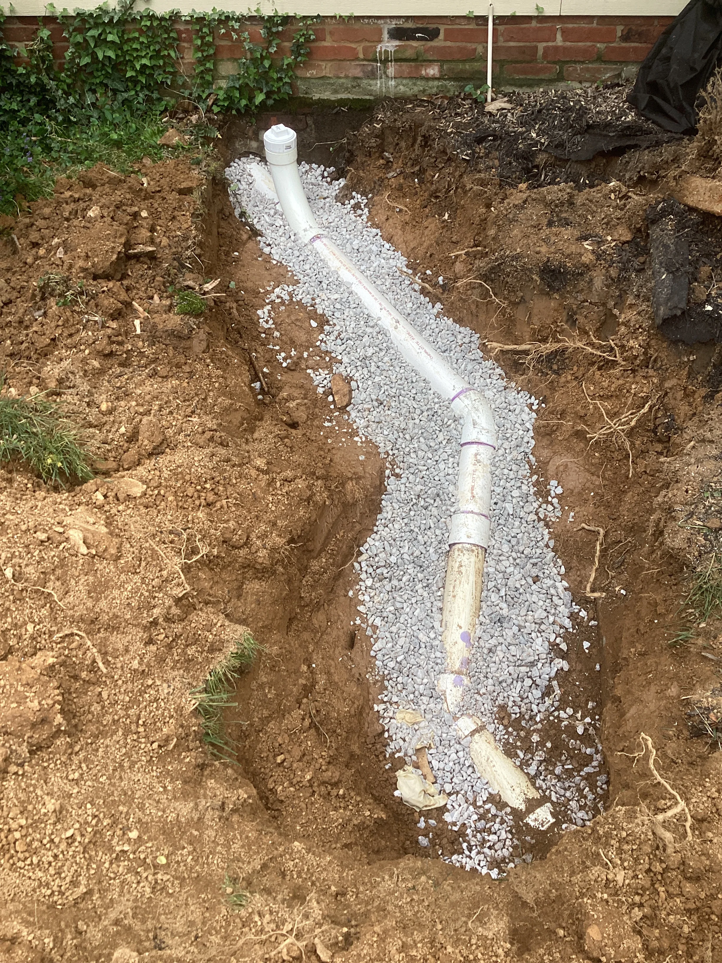Underground PVC drainage pipe installation with white gravel bedding in excavated trench