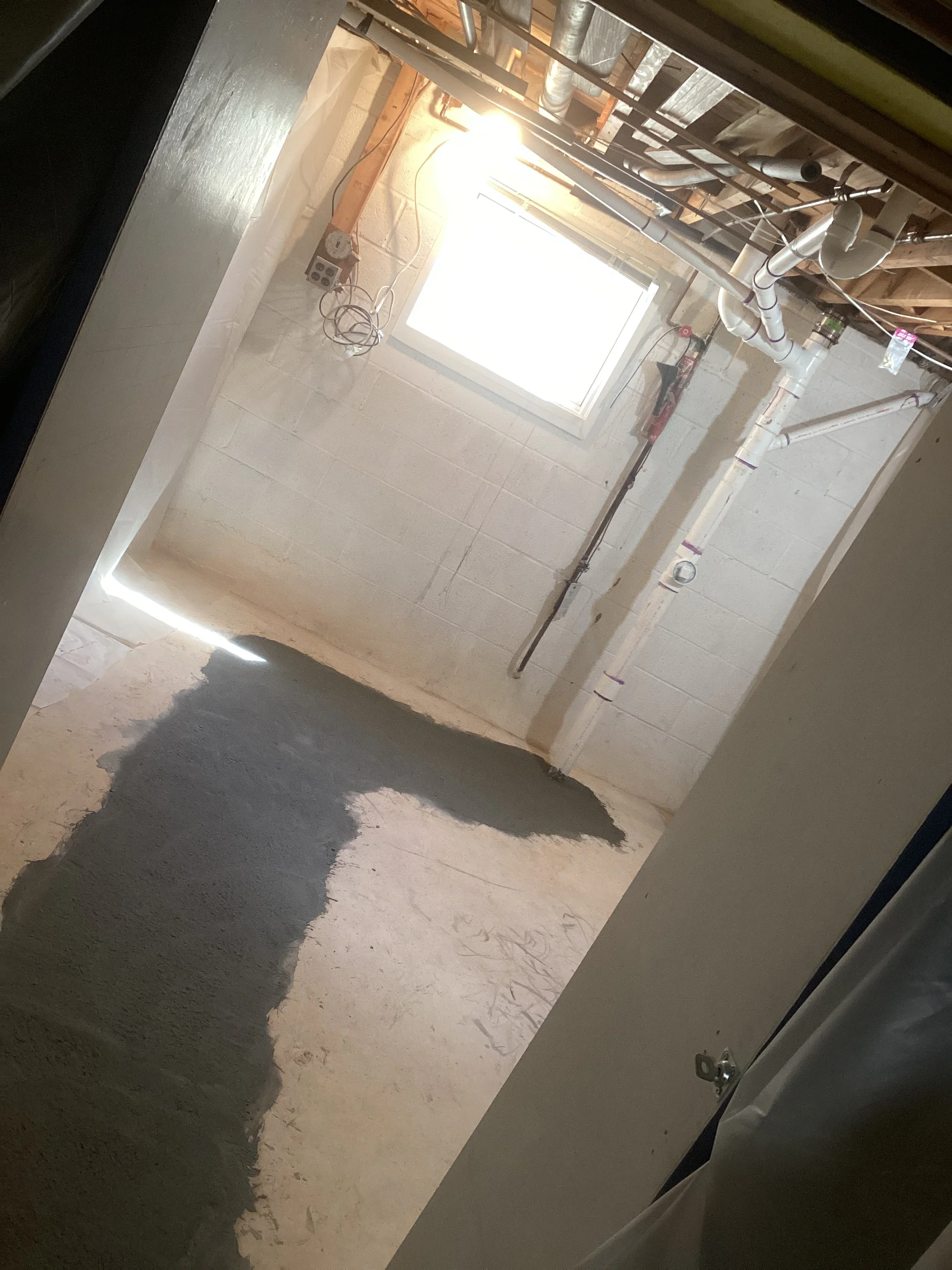 Basement plumbing installation with PVC pipes, concrete floor, and skylight opening