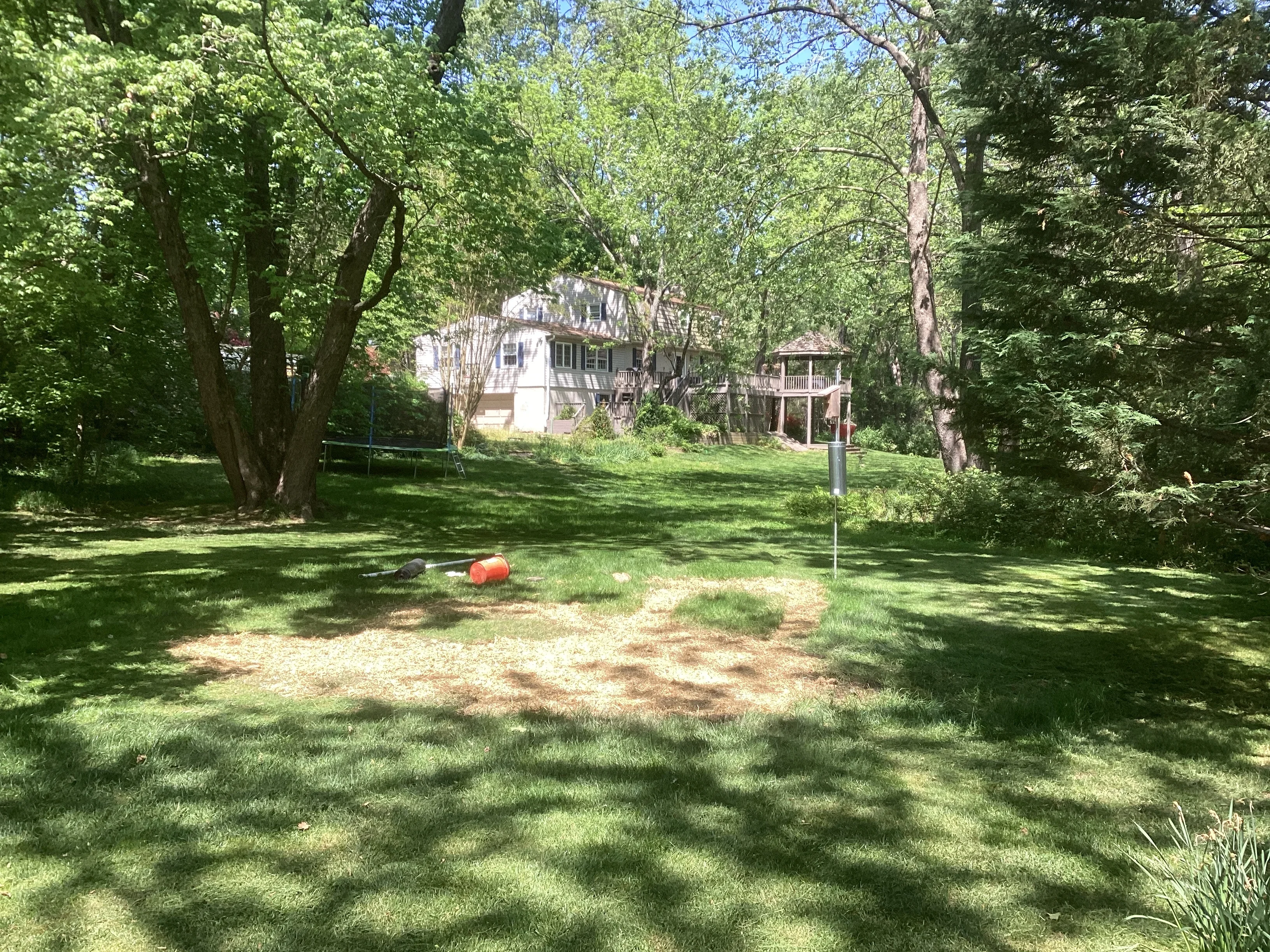 Residential yard with drainage installation, gravel base, and mature trees surrounding home