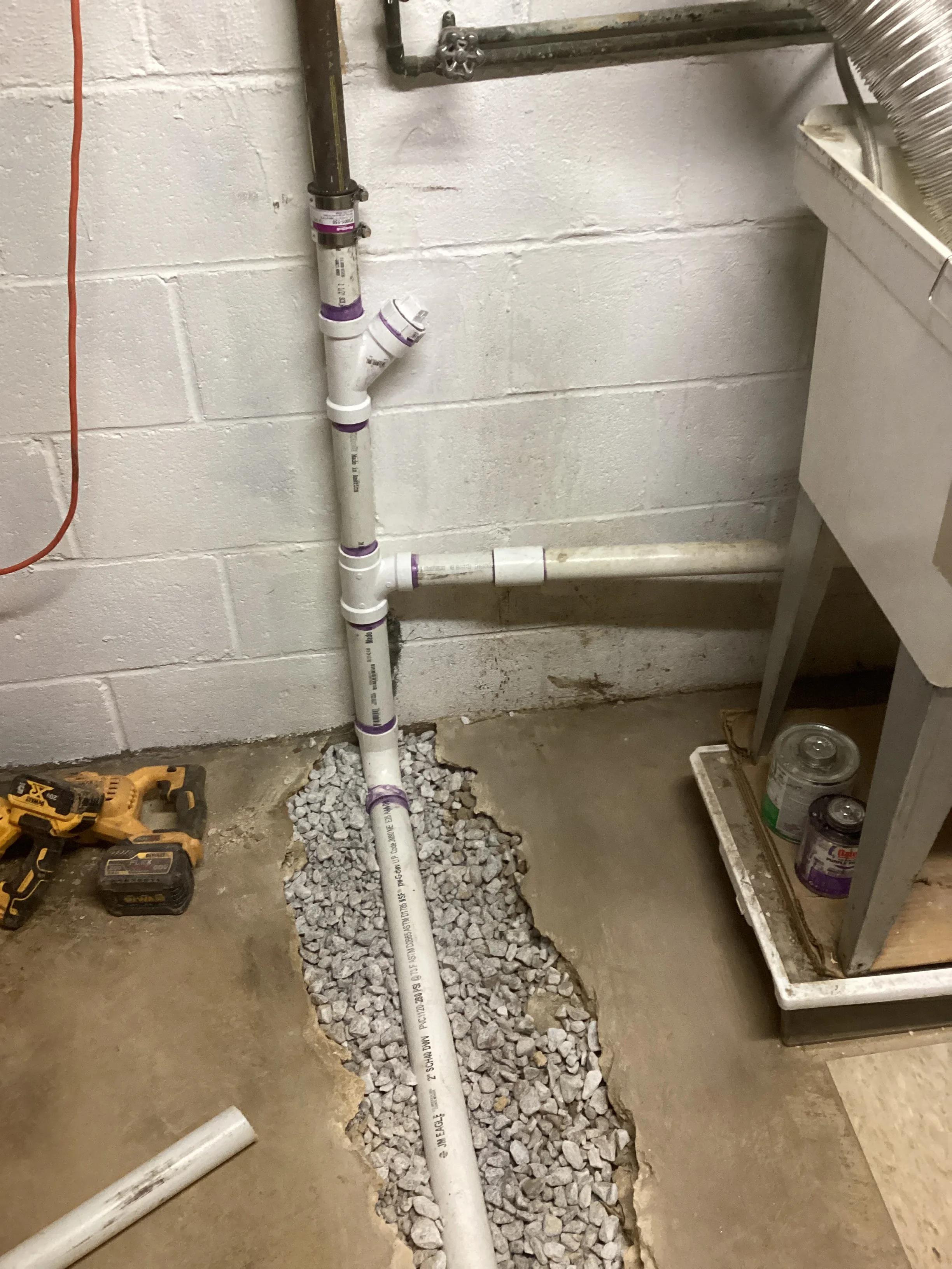 New white PVC drain pipe installed in basement with gravel bed and wall-mounted connections