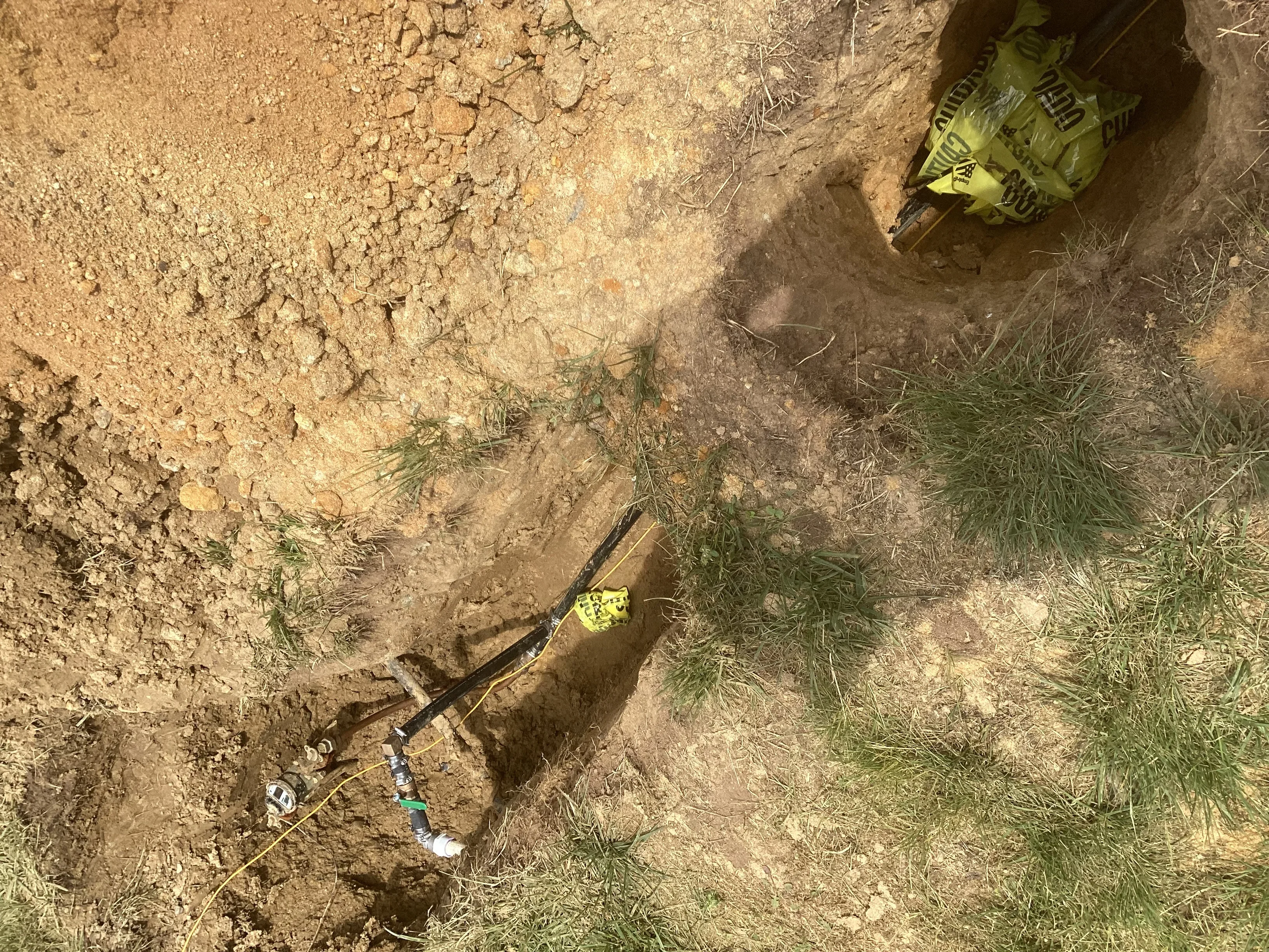 Underground drainage pipe installation in excavated trench with yellow safety equipment visible