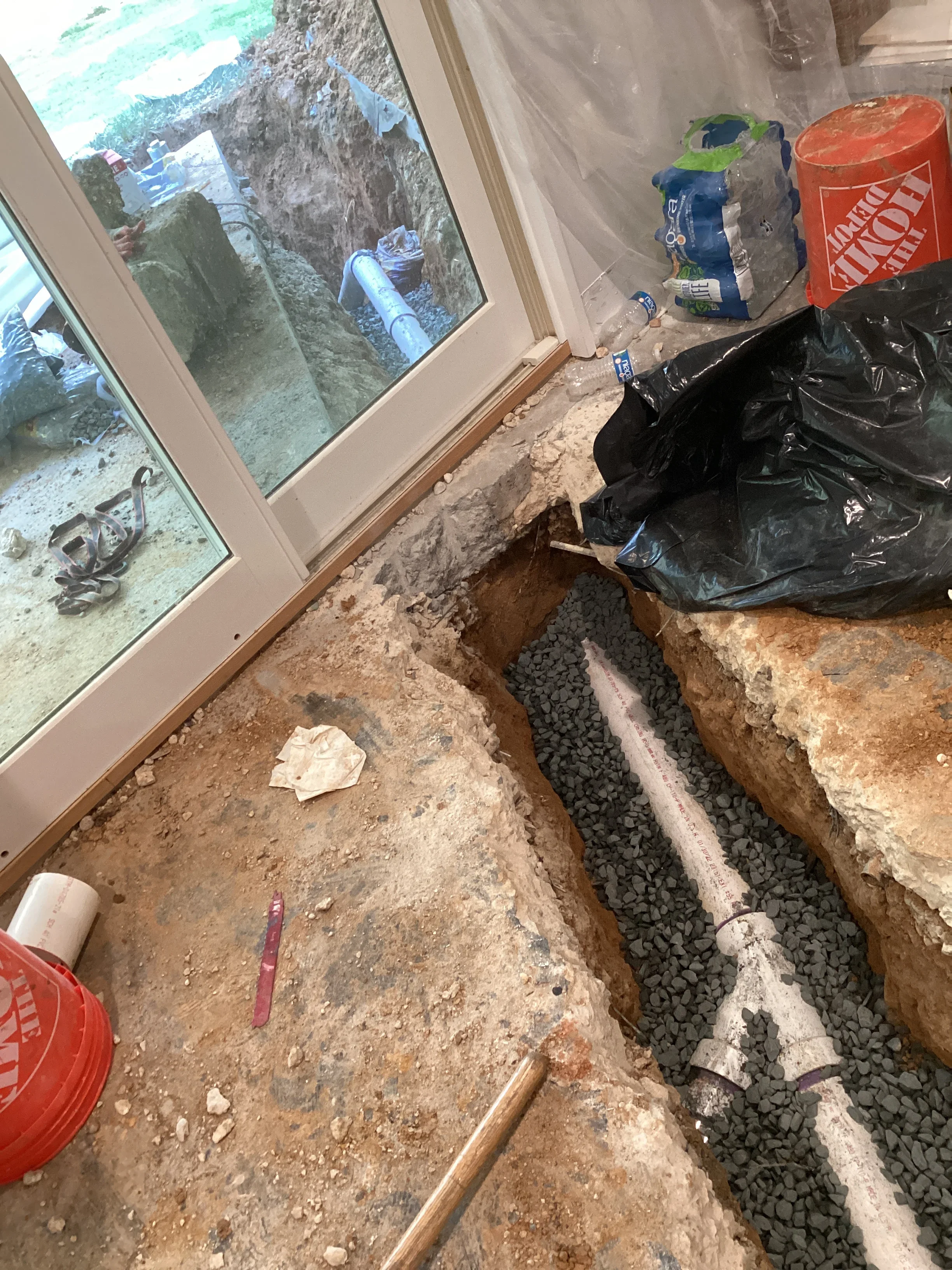 Underground drainage pipe installation in excavated trench with gravel bedding and concrete collar