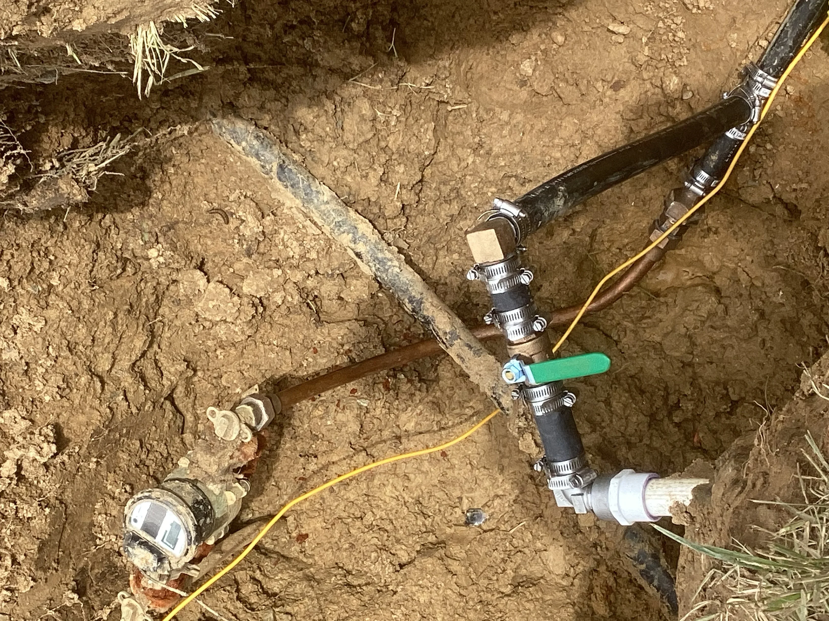 Underground water line repair with PVC pipe, brass valves, and yellow tracer wire in trench