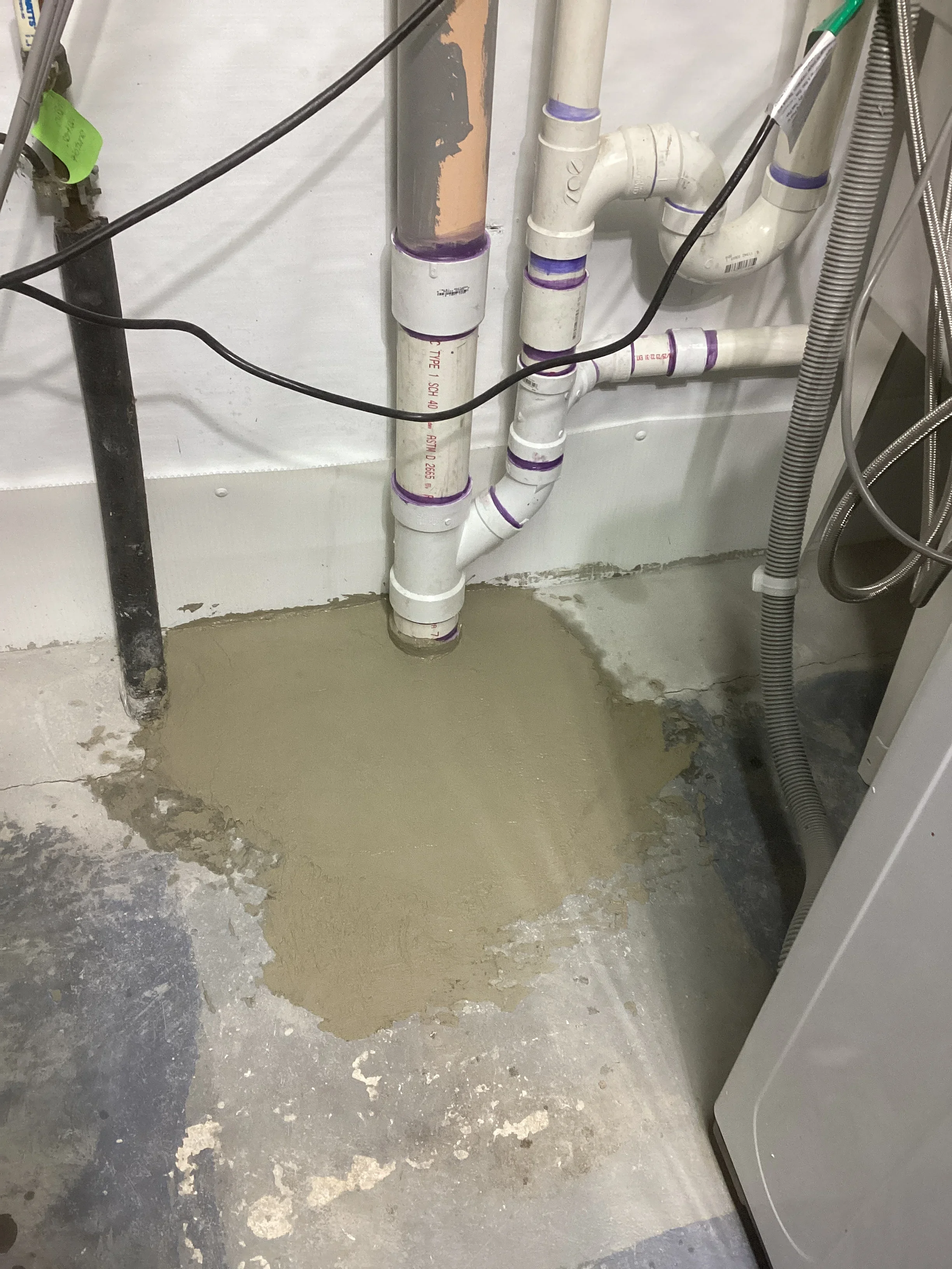 Installed basement sump pump system with white PVC piping and purple couplings in concrete basin