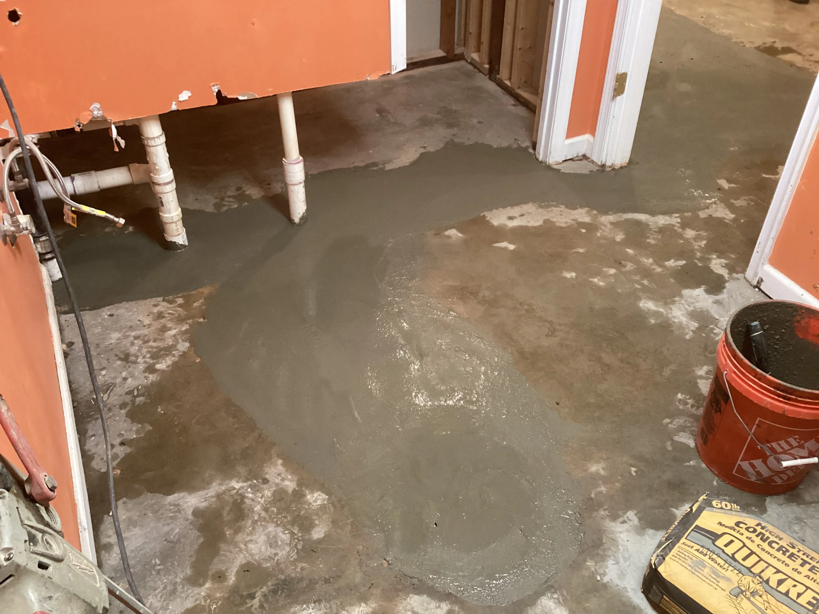 Wet concrete floor with PVC pipes and protective barriers during plumbing installation prep