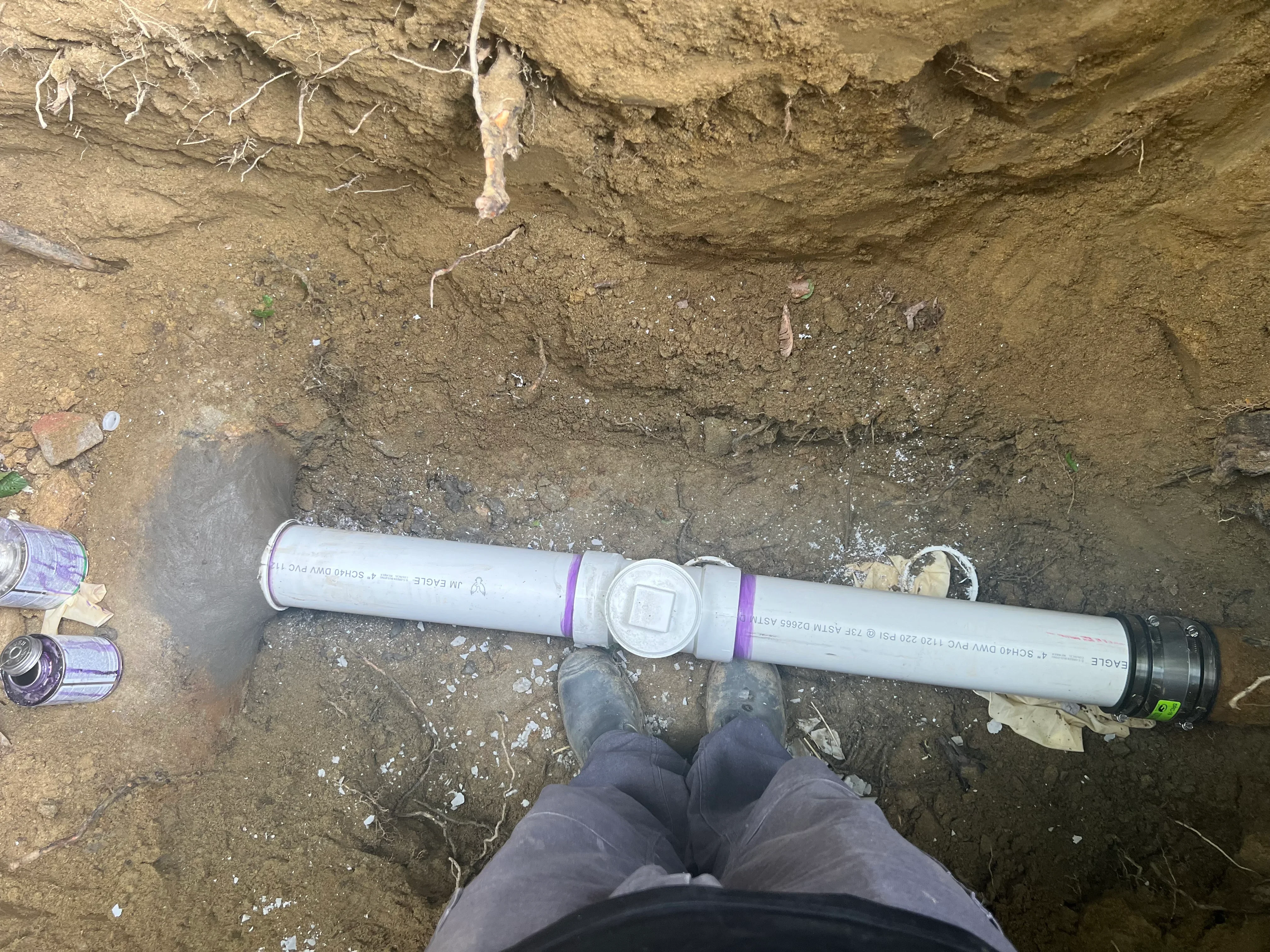 White PVC sewer pipe with purple couplings installed in excavated trench during underground utility work