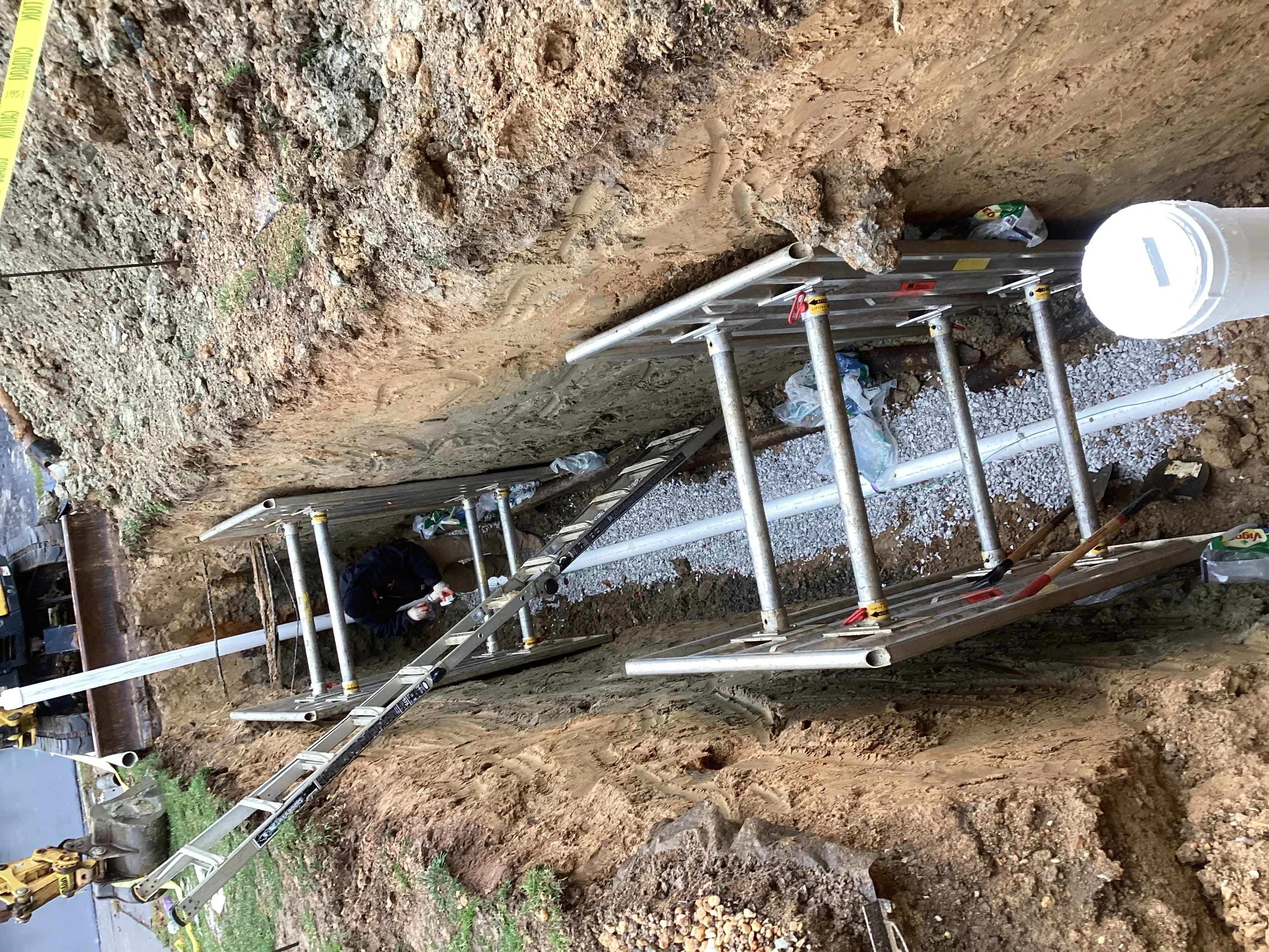 Underground sewer line installation with metal supports and gravel bedding in excavated trench