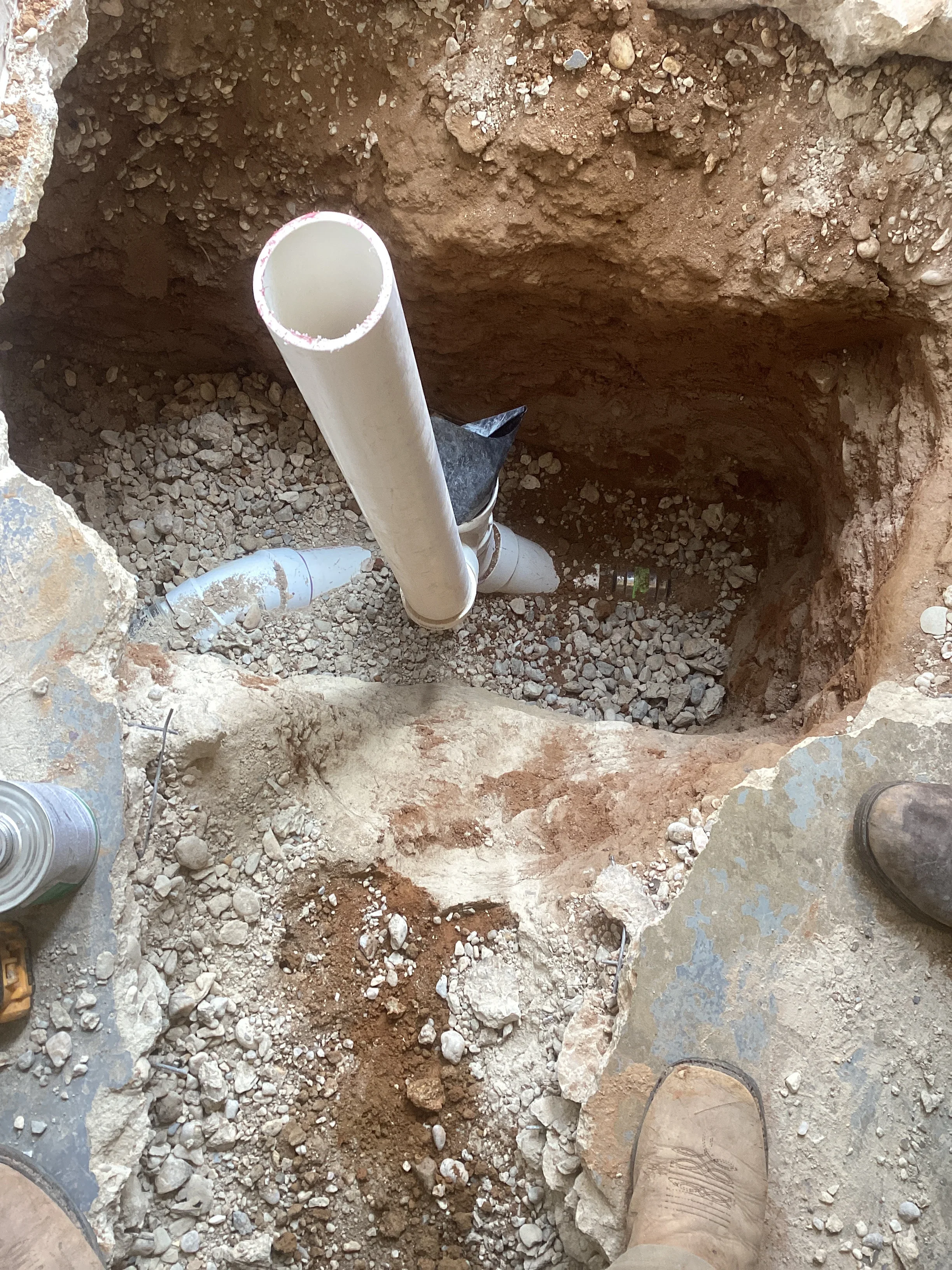 White PVC drainage pipe installed in excavated trench with gravel base and surrounding soil