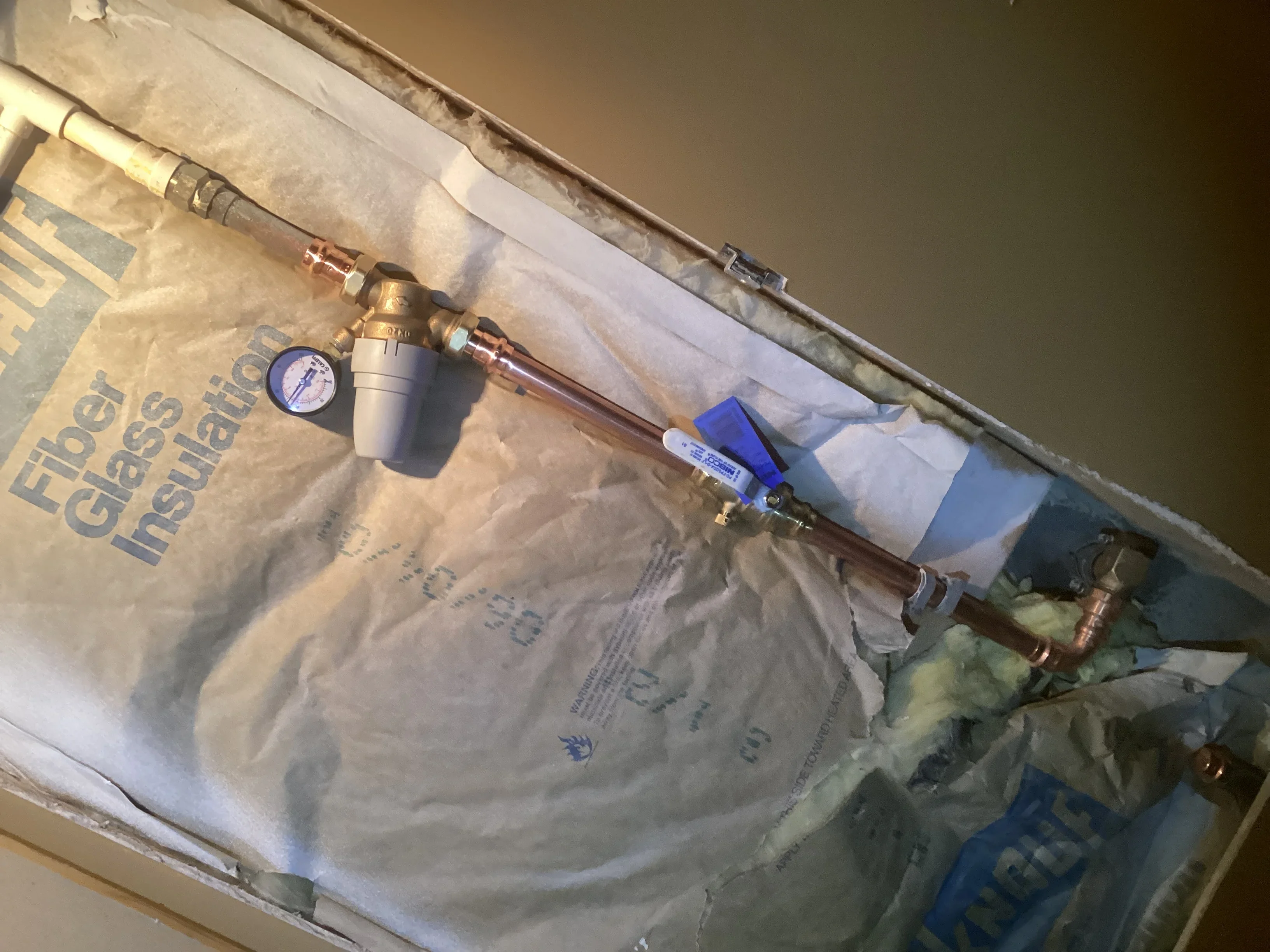 Copper water line with pressure gauge, shutoff valve, and blue insulation wrap installed in attic space