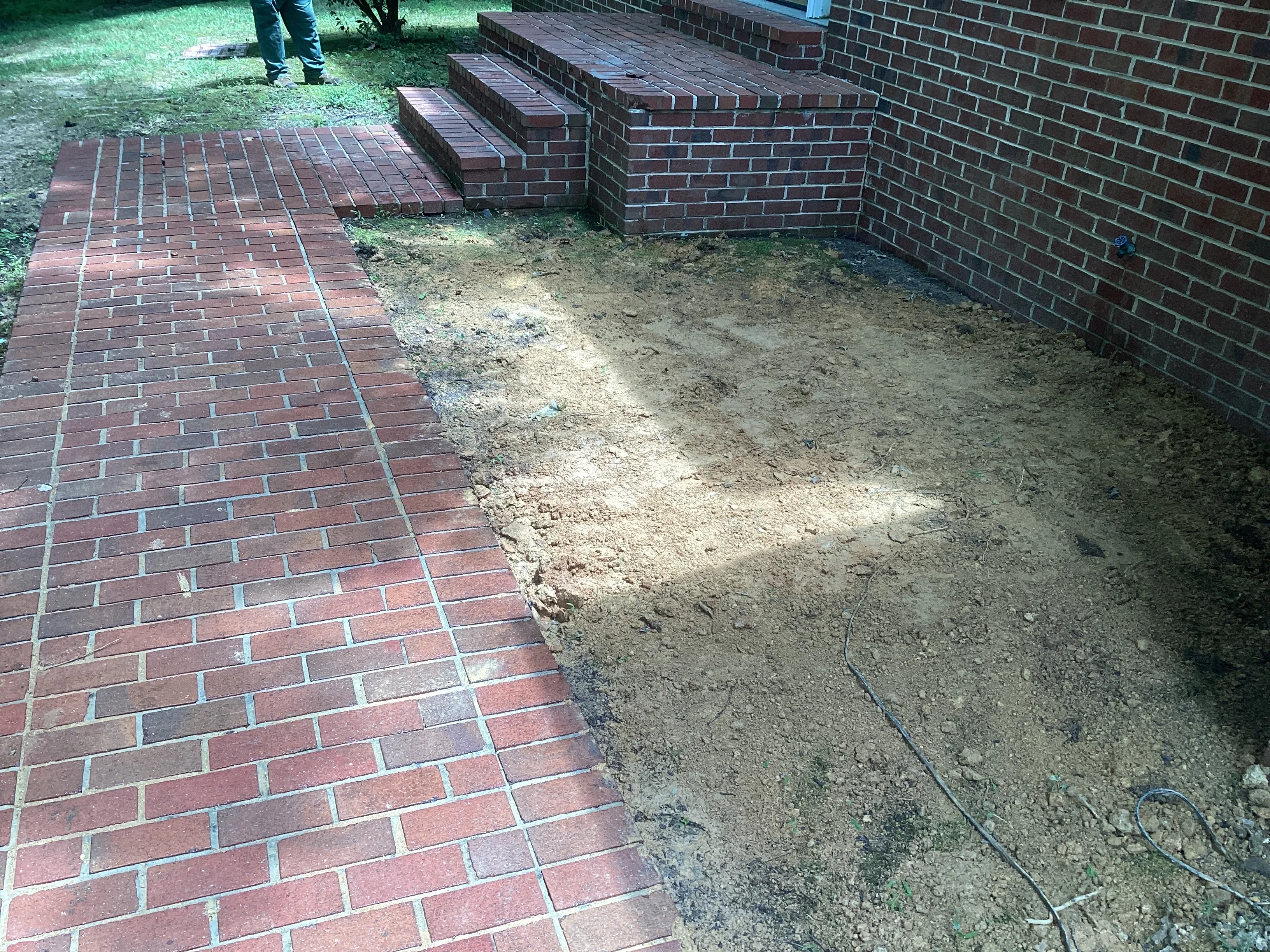 Excavated yard area next to brick home foundation with exposed soil and brick patio edge