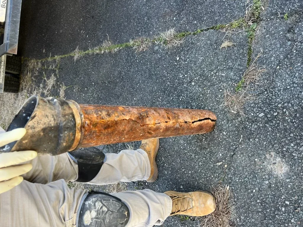 Technician holding corroded cast iron sewer pipe with heavy rust damage and cracks