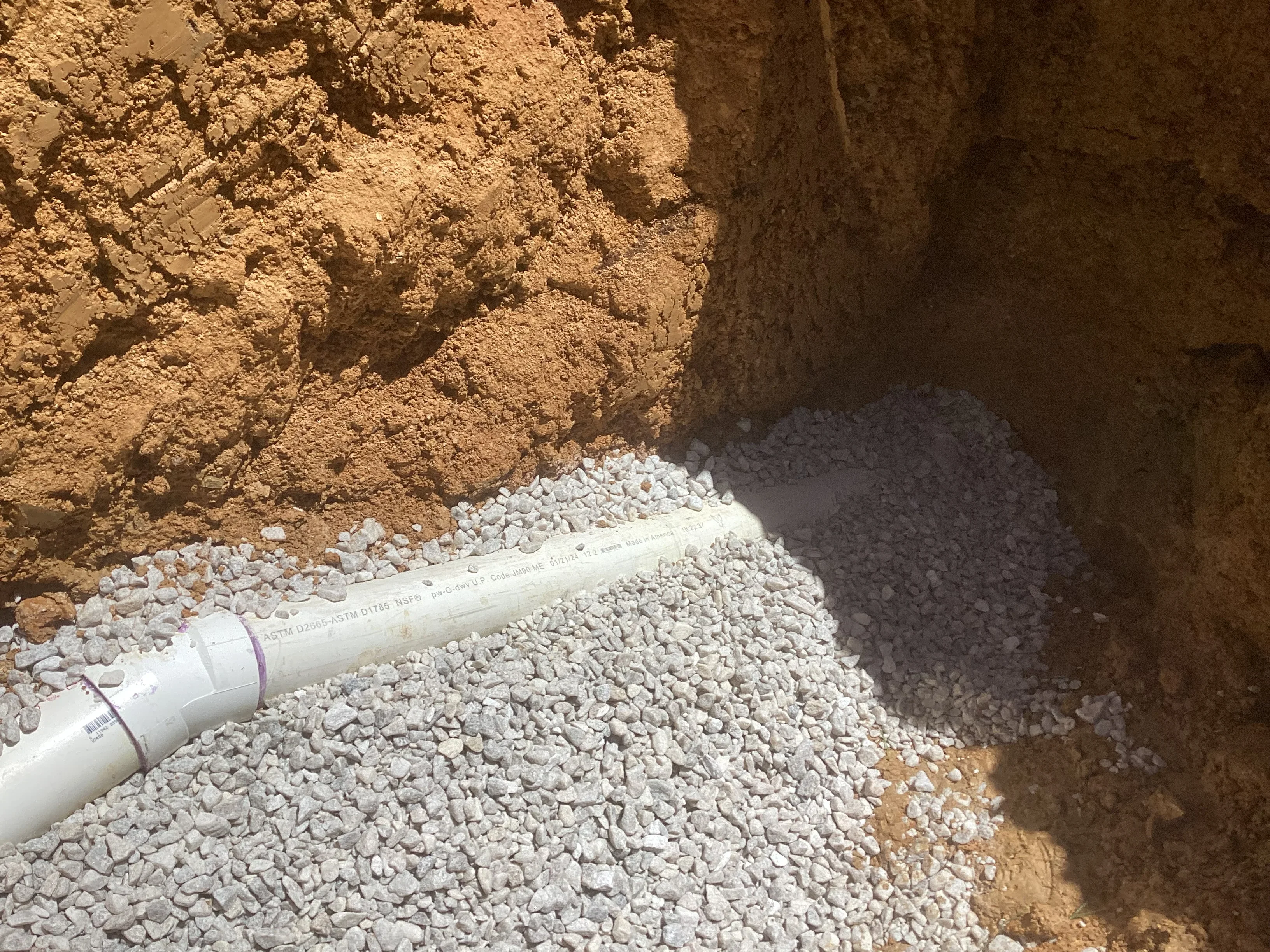 PVC drainage pipe installed in gravel-lined trench with compacted soil walls