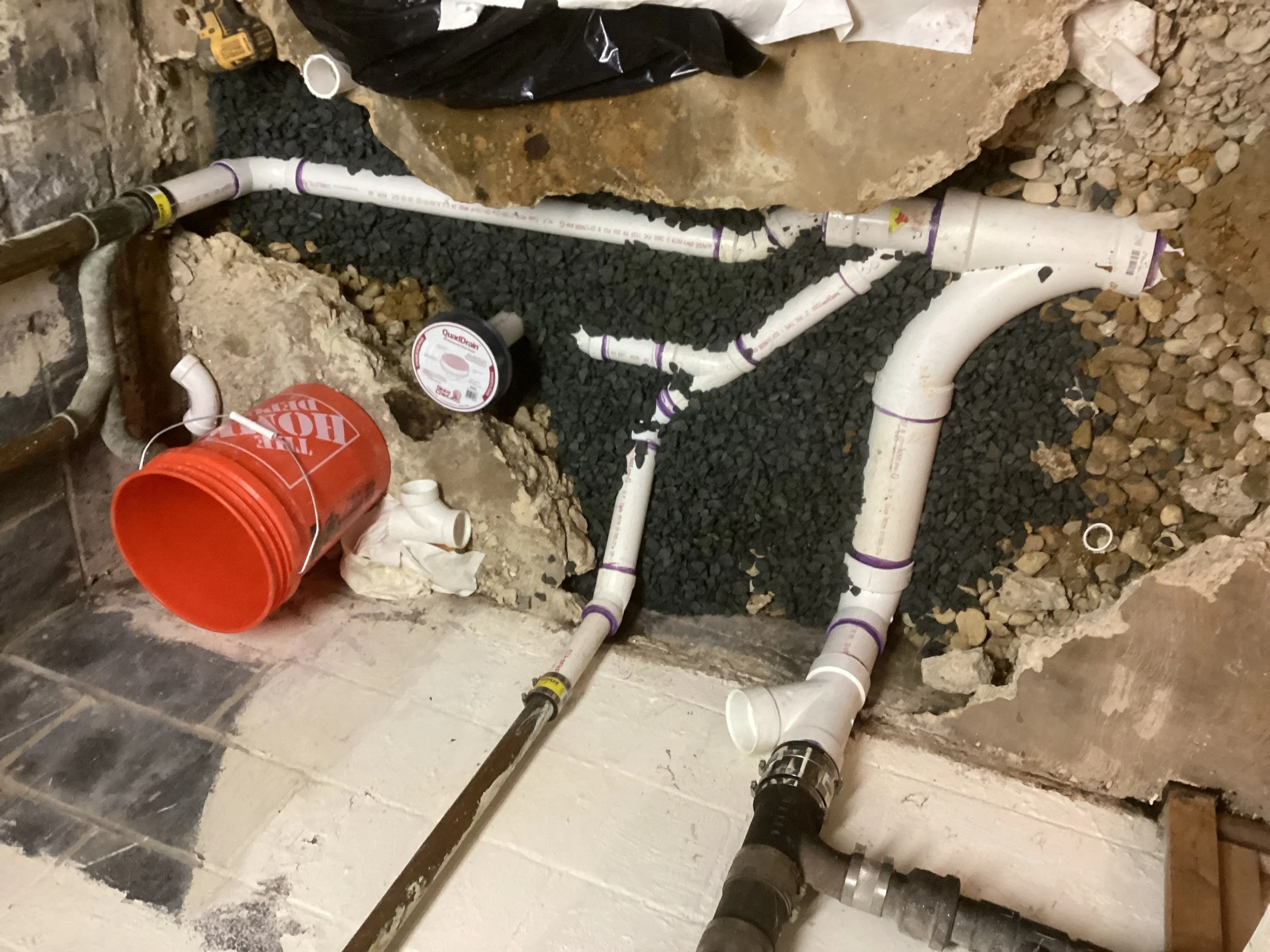 Basement plumbing installation with white PVC pipes, red bucket, and foundation work