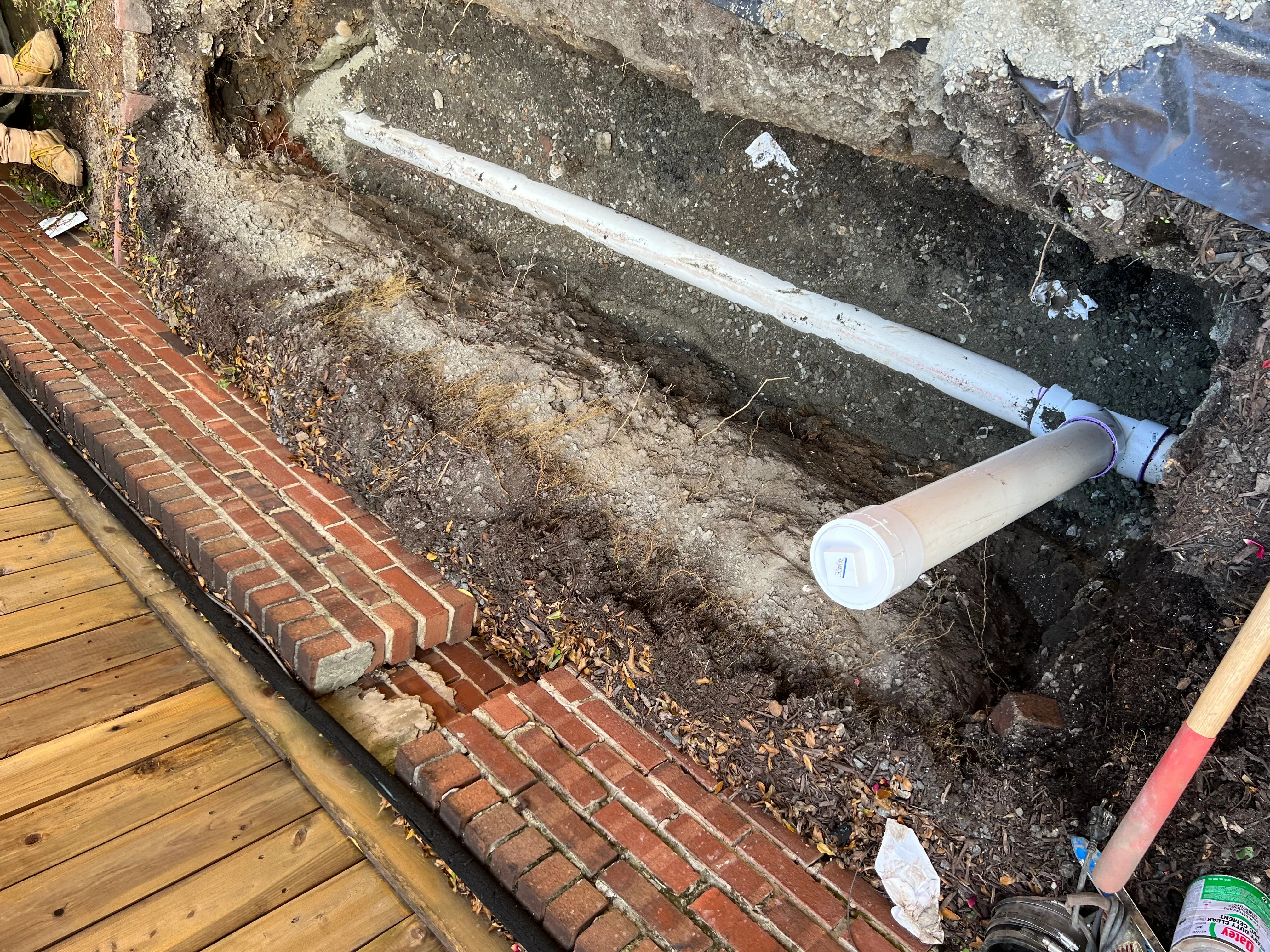 Underground drainage pipe installation in excavated trench next to brick foundation