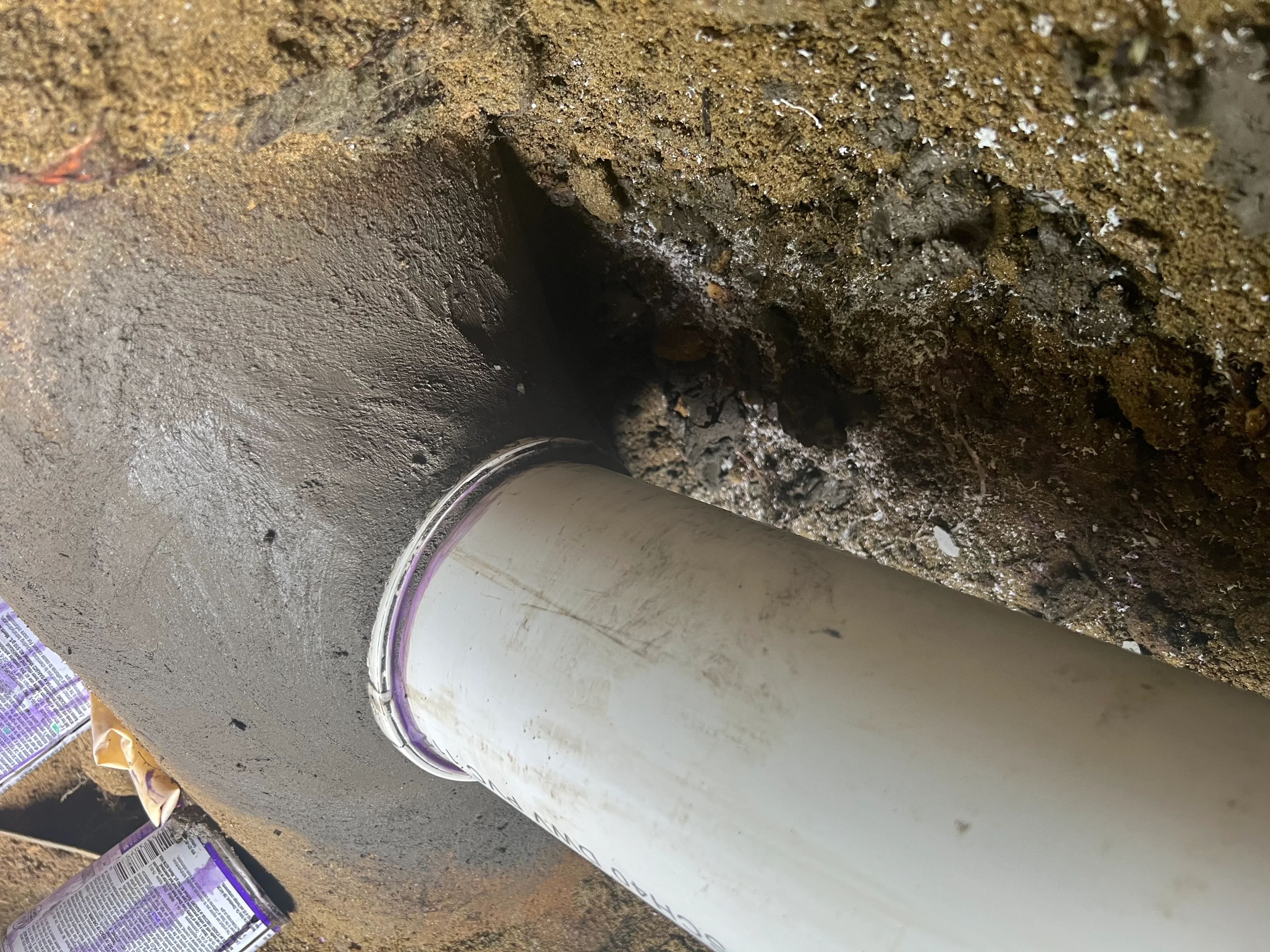 White PVC sewer pipe with purple marking installed in underground trench with compacted soil