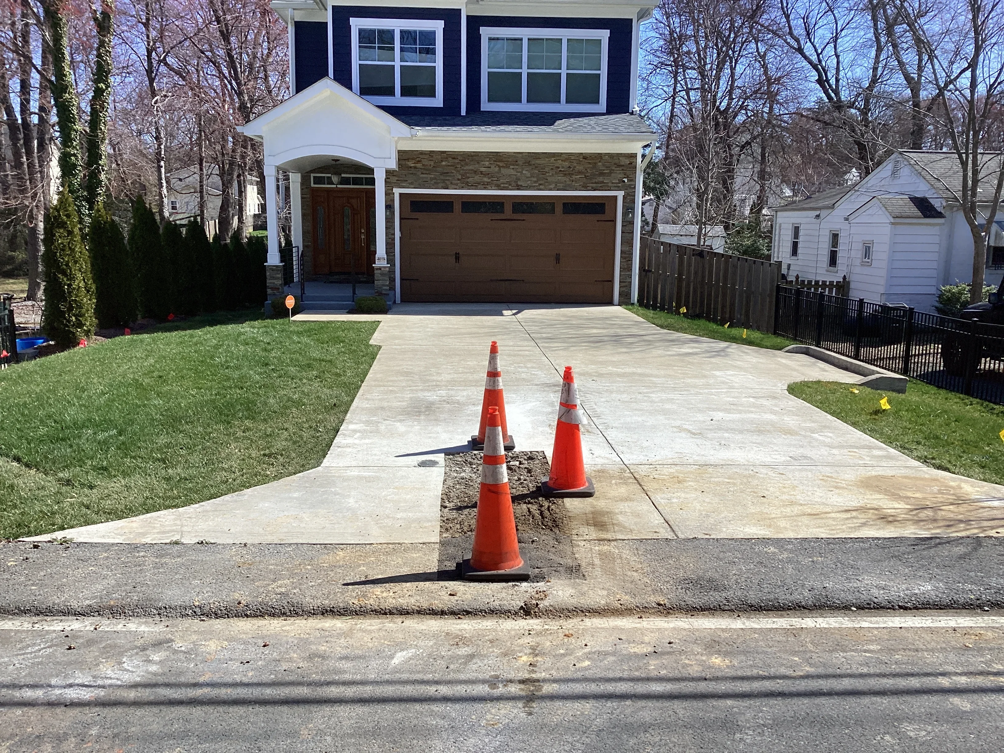 New concrete driveway with utility line installation marked by traffic cones
