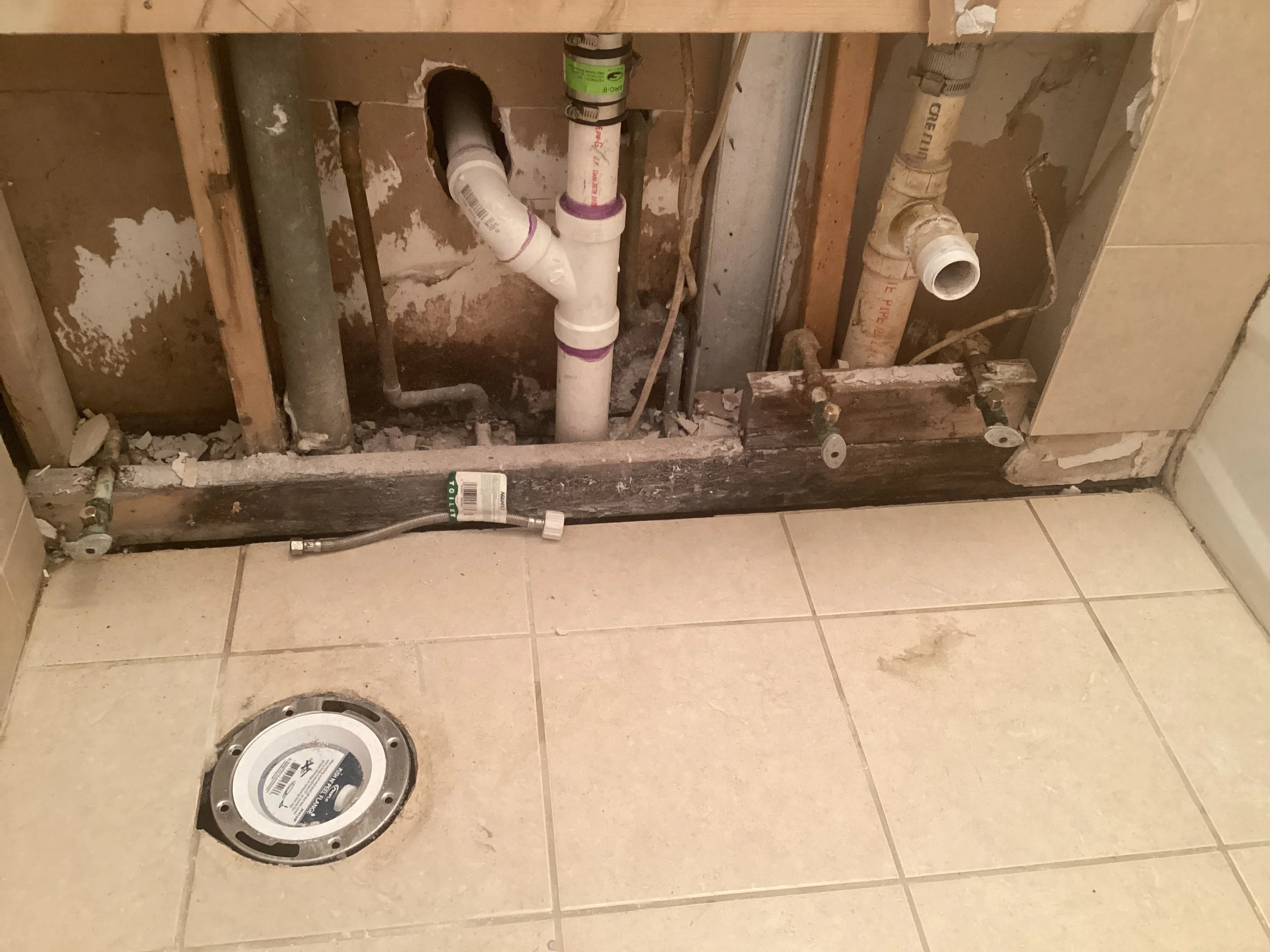 Bathroom subfloor plumbing with white PVC pipes, drain assembly, and new supply lines installed