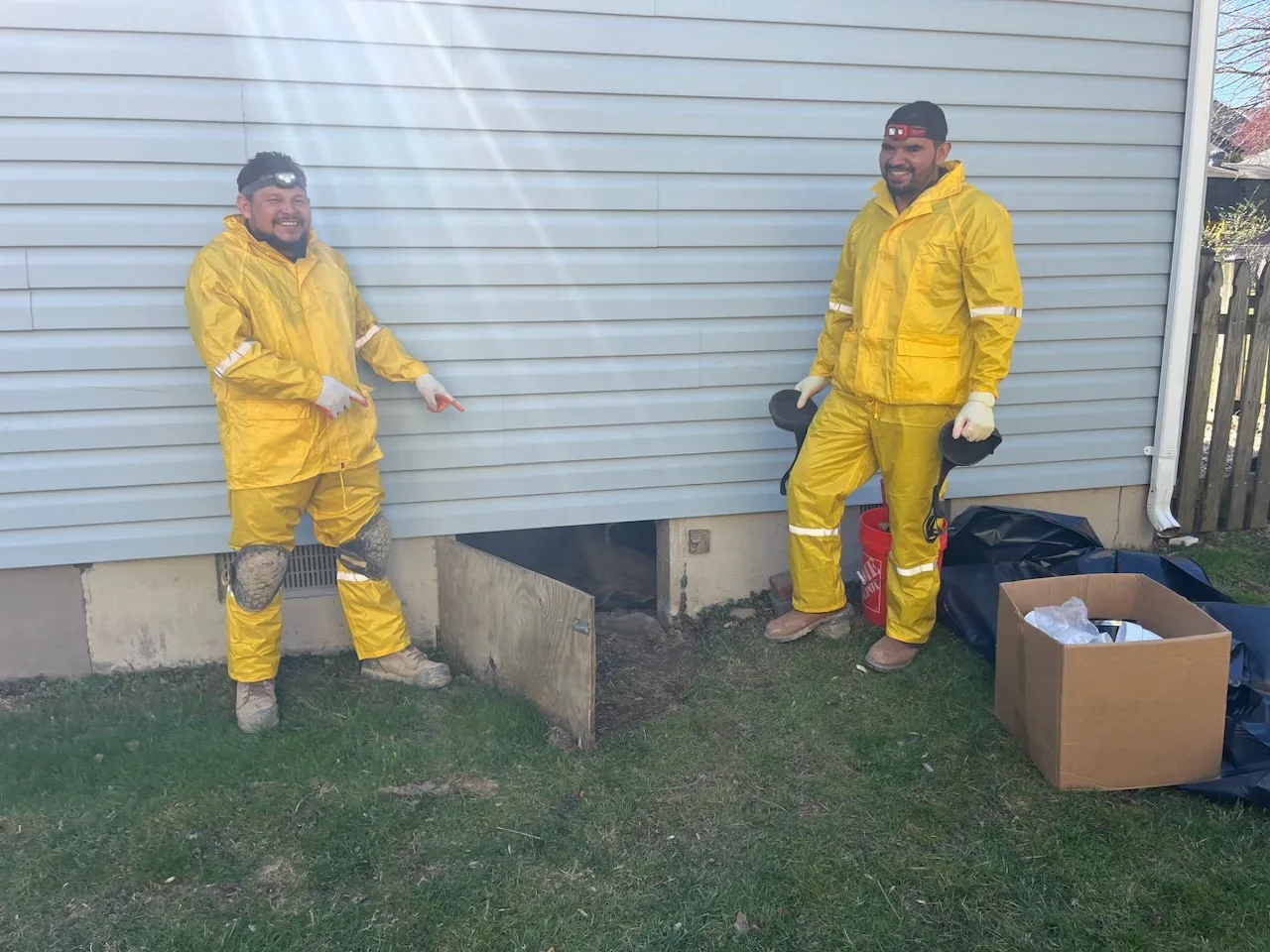 Two technicians in yellow protective suits standing at foundation drainage installation site