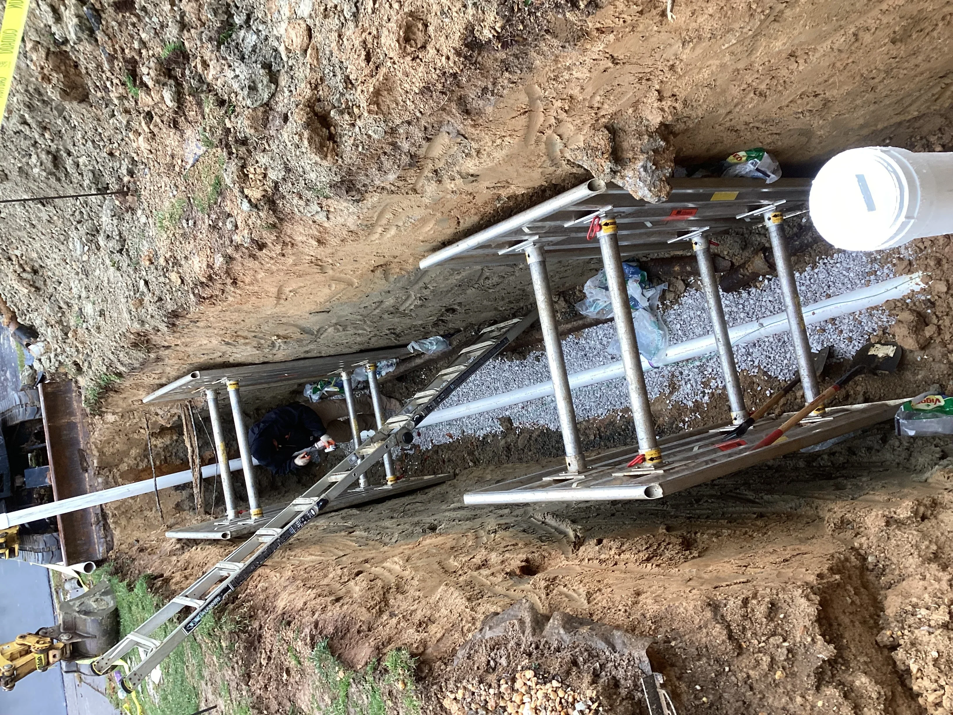 Underground PVC pipe installation with steel supports and gravel bedding in excavated trench