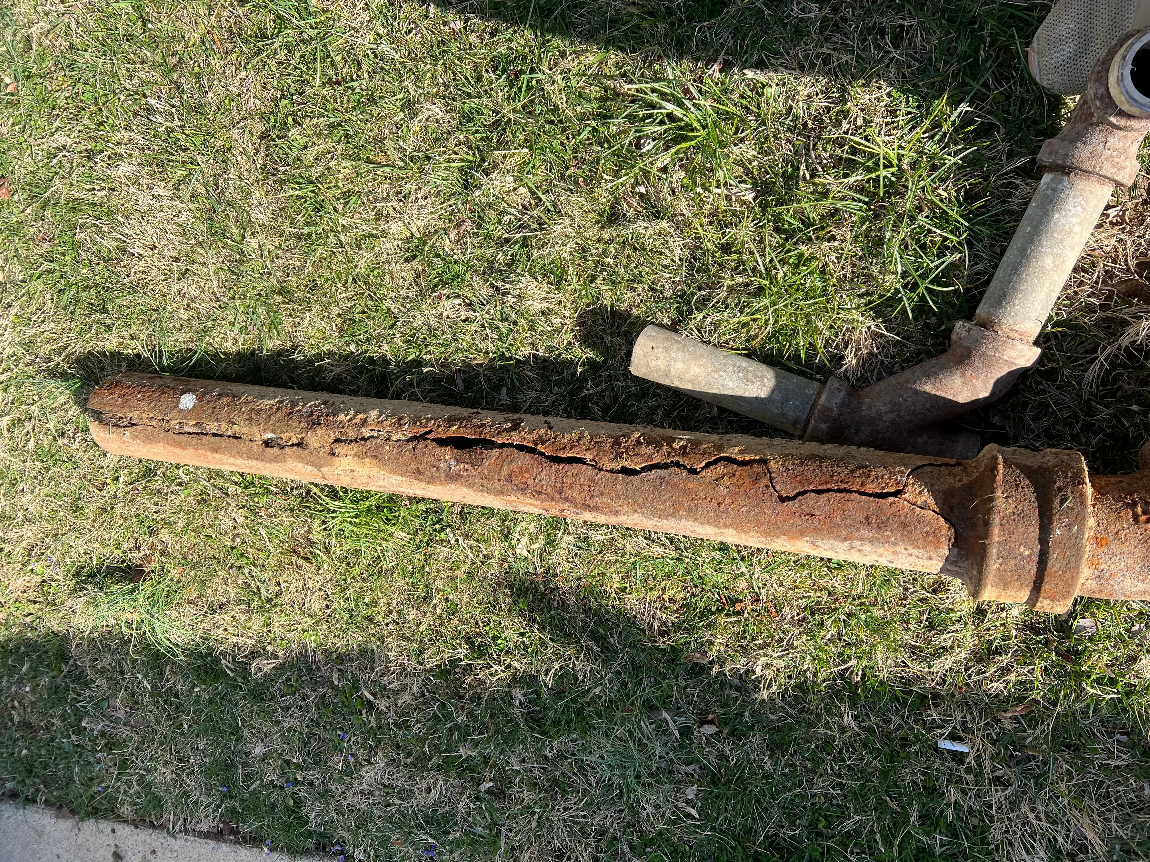 Corroded cast iron sewer pipe with deep rust damage and cracks exposed during excavation
